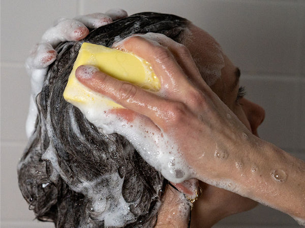 Frau schäumt ihre Haare mit festem Shampoo von Duschbrocken ein.